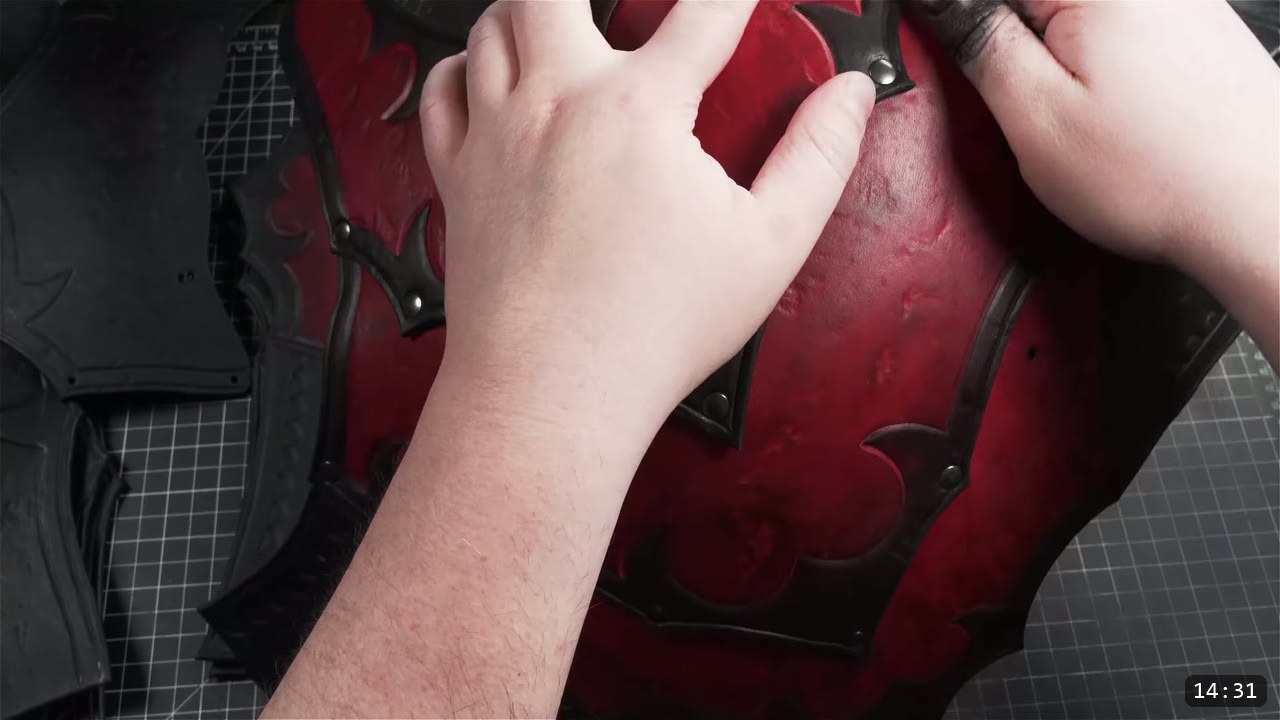 hands pressing the domed red front plate, its black barbed border riveted along the edge