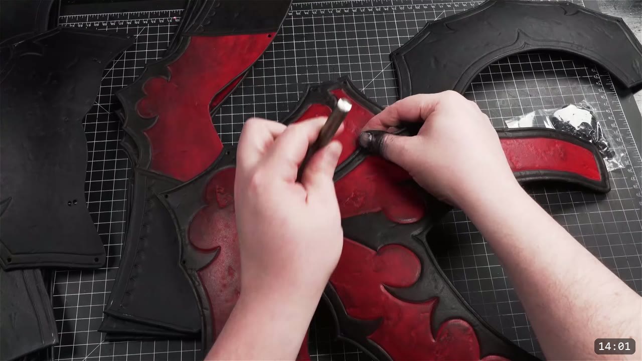 two hands setting a rivet with a small metal setter on the domed red and black front plate, all-black back pieces and a bag of rivets nearby