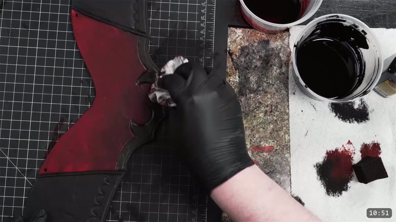 a gloved hand buffing a rag across the dyed red and black plate, with cups of red and black dye and a sponge on the bench