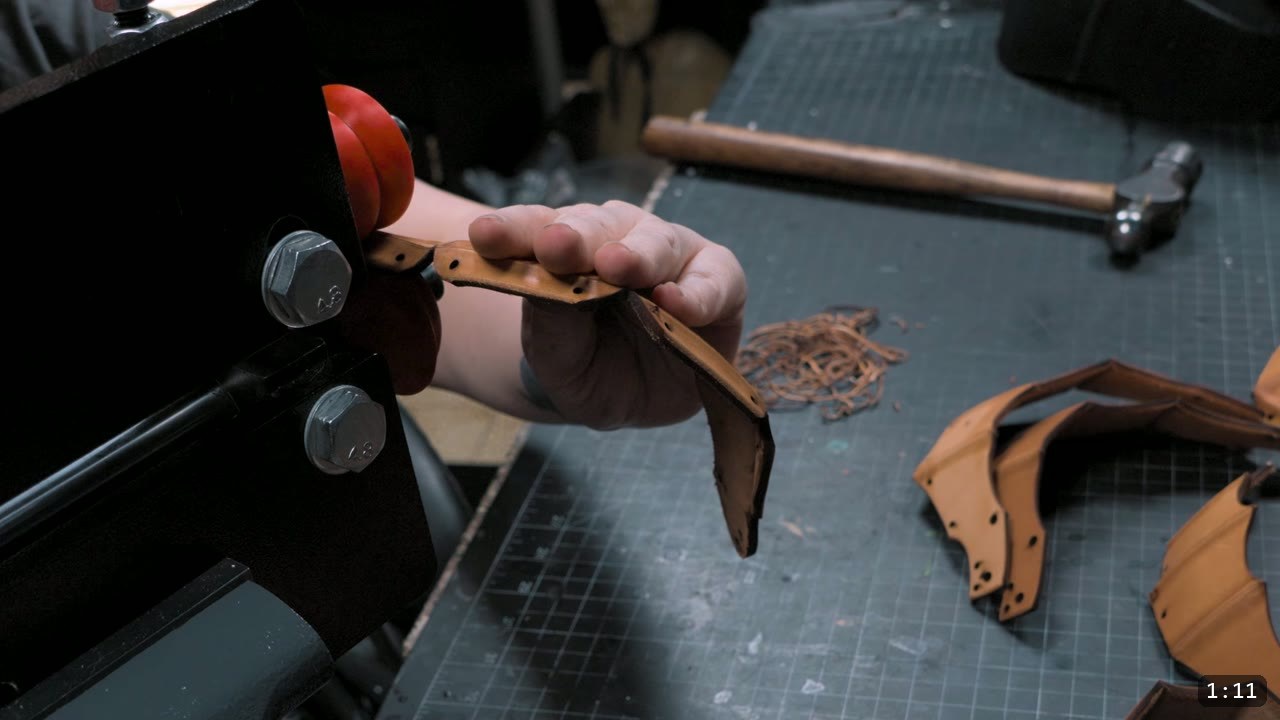 holding a freshly cut natural vegetable-tan elbow piece at the bench, cut articulated lames resting on the cutting mat