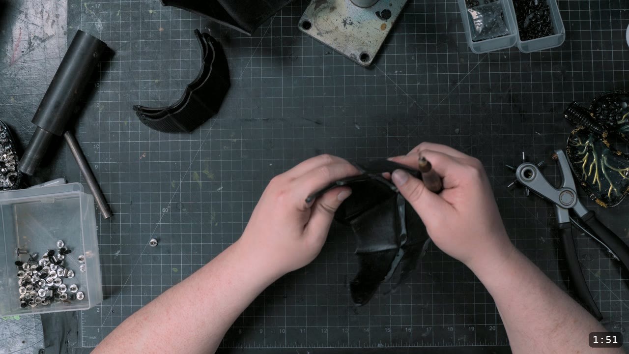 lining up the rivet holes on a dyed-black elbow piece, double-cap rivets and a rotary punch on the cutting mat
