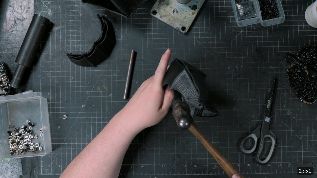 setting a double-cap rivet on the dyed-black elbow shell with a ball-peen hammer over a steel post