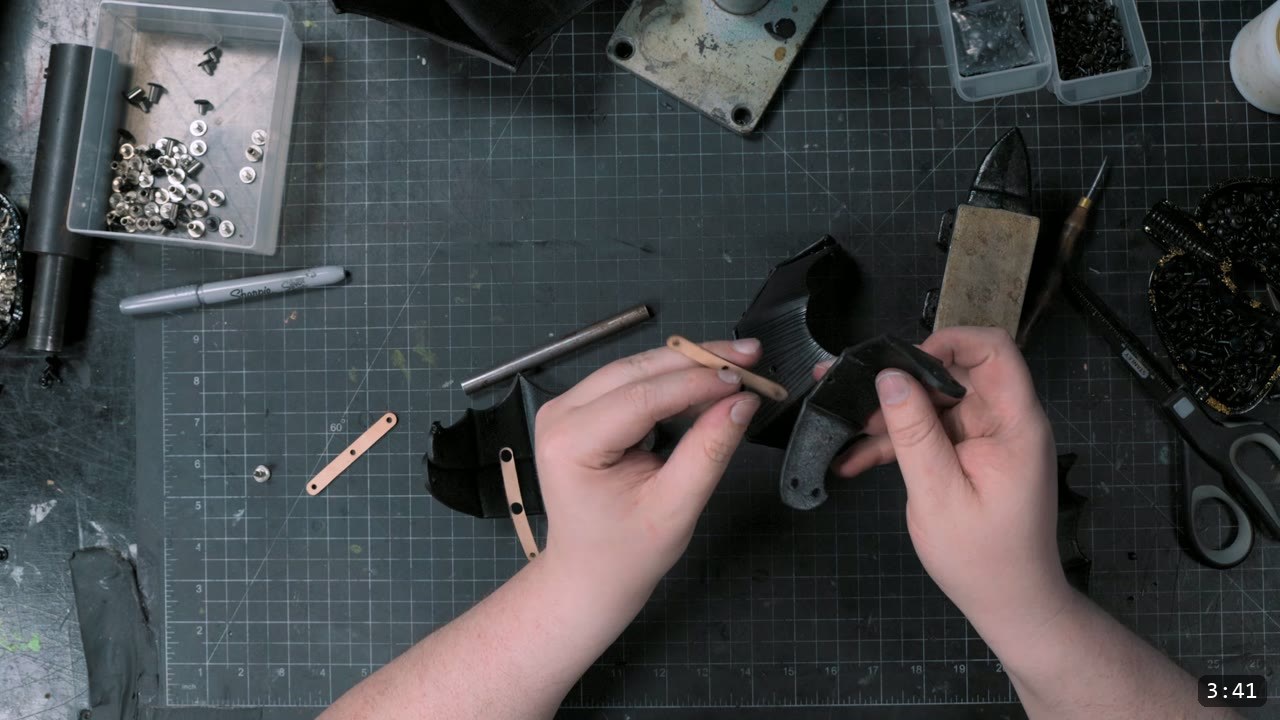 connecting two dyed-black lames with a retaining strap, a metal setting post and awl on the bench