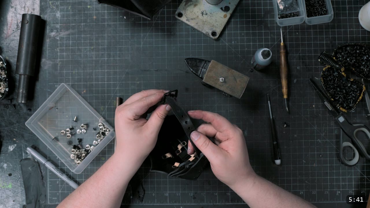 riveting the strap that spans the inner elbow to hold the couter in position