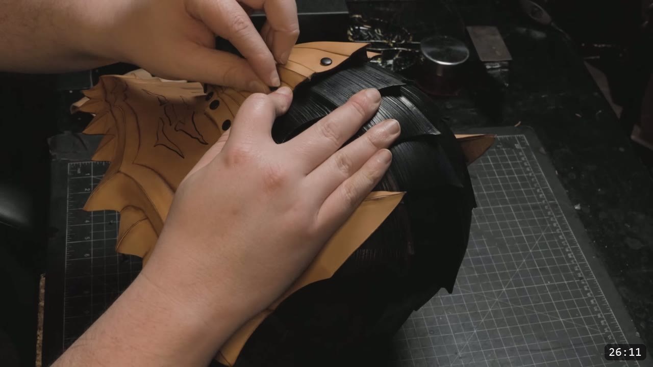 hands fitting a natural-tan carved faceplate against the dyed-black fluted crown of the helmet