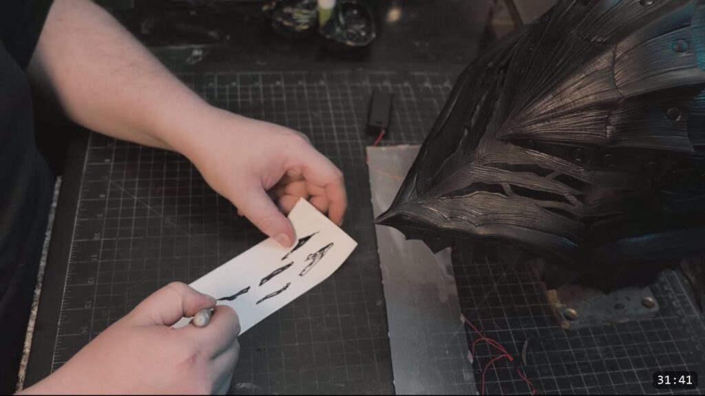 a hand holding a small printed reference beside the finished black faceplate with its striated texture