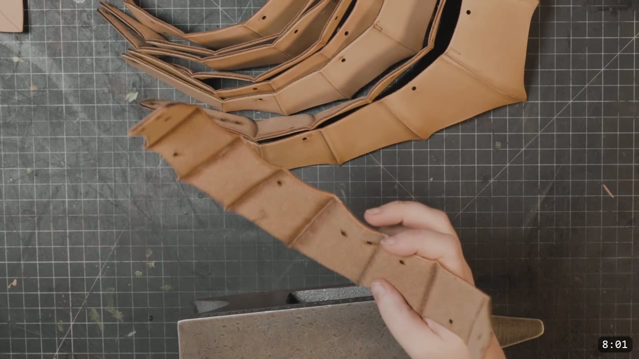 a fan of tan helmet plates with raised fluted ridges embossed into them, one strap being worked over a stone block
