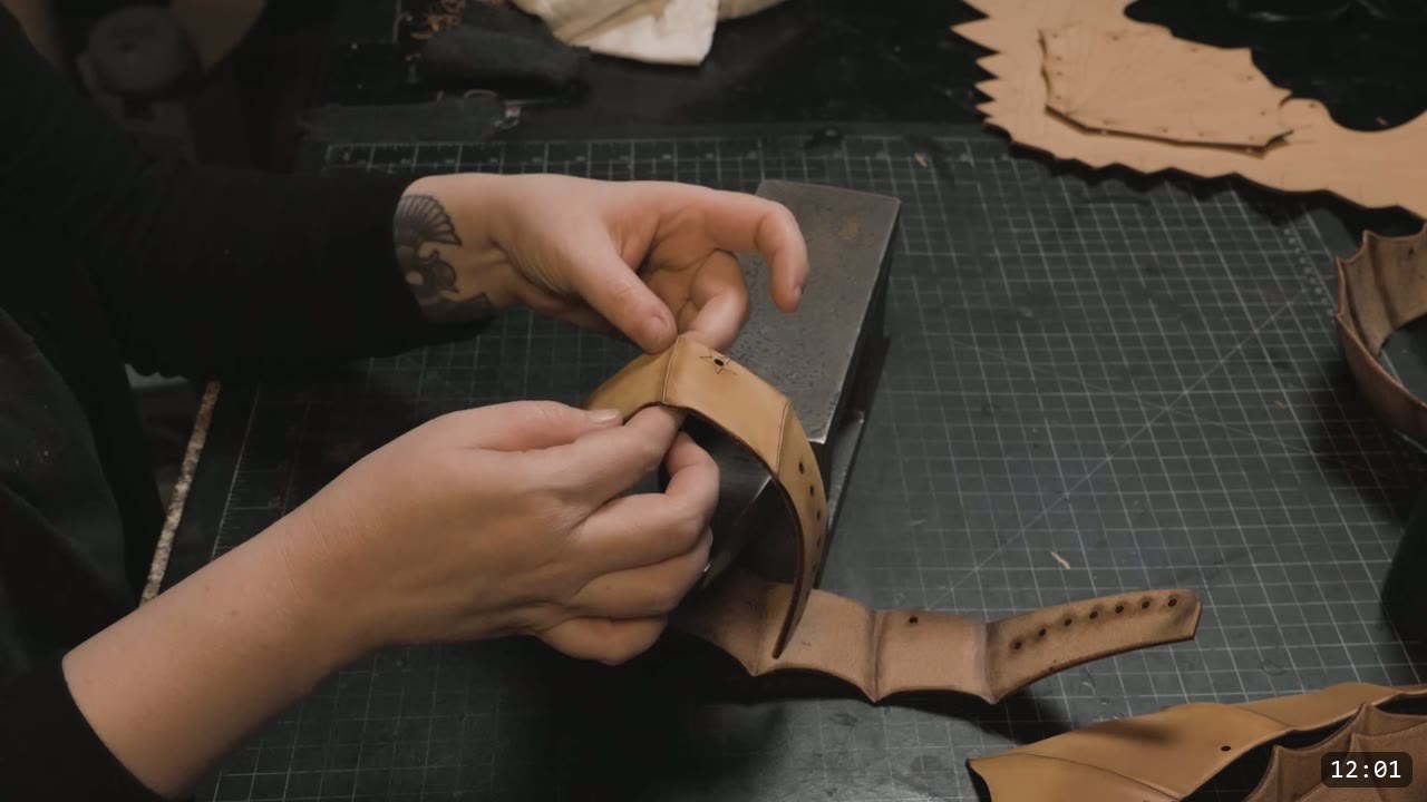 pressing a small curved leather plate to shape over a steel bench block, more fluted plates and cut sheets nearby