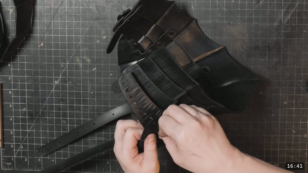 hands fitting dyed-black fluted plates together during core assembly, a punched black retaining strap resting at left