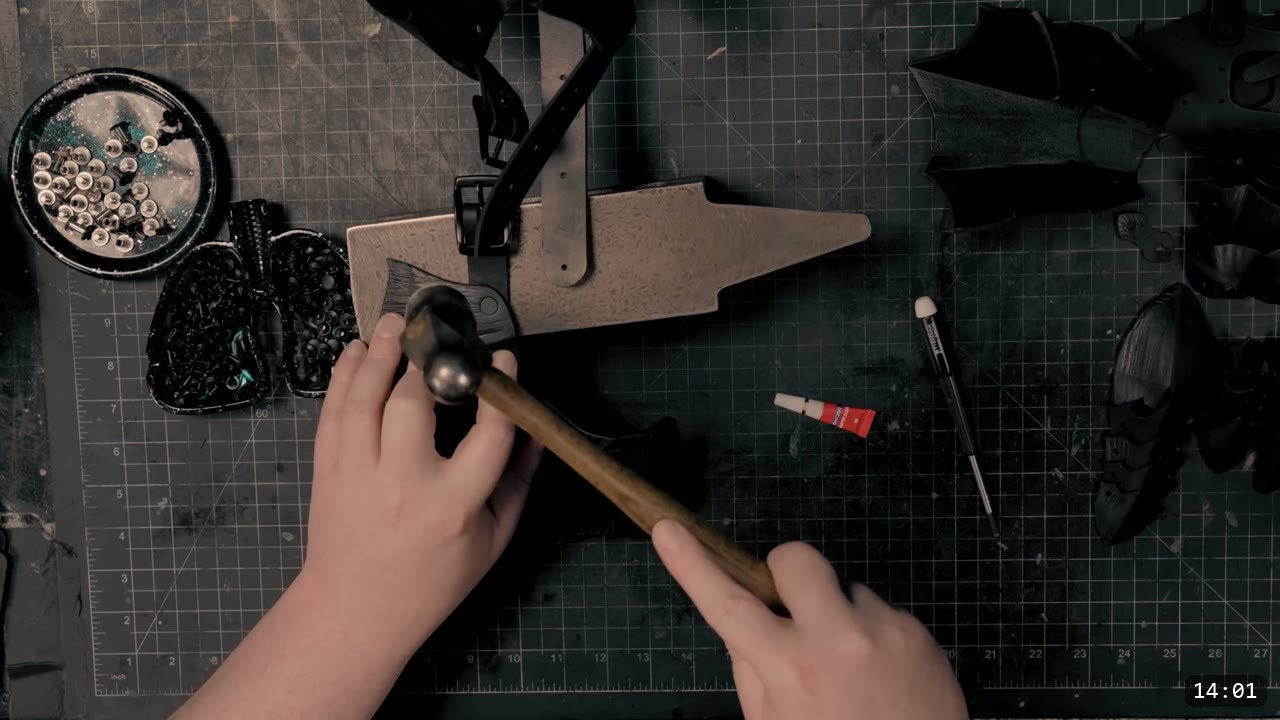 Berserk Gauntlets Build Guide: The Leather Version, Step by Step 11 a hand with a ball-peen hammer and a pointed mini anvil setting rivets on a black buckle strap, a tray of silver rivets and a tube of thread lock nearby