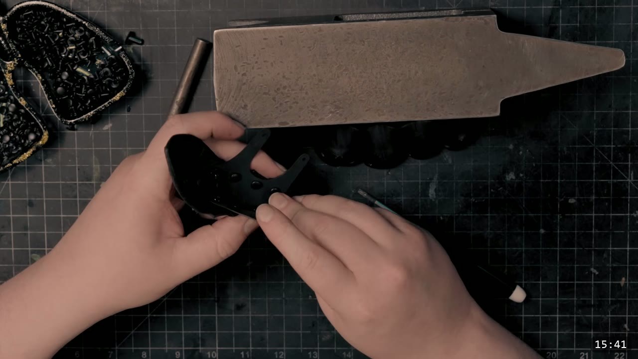 Berserk Gauntlets Build Guide: The Leather Version, Step by Step 12 hands riveting a small black dyed thumb piece against a pointed mini anvil, a tray of black hardware alongside