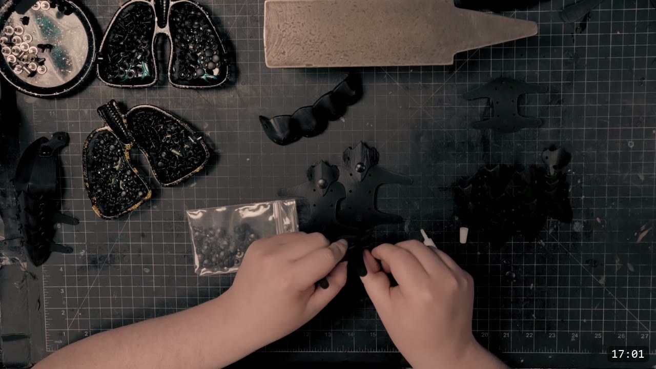 Berserk Gauntlets Build Guide: The Leather Version, Step by Step 13 hands setting small rivets on black dyed finger scale pieces, bags and trays of black hardware on the cutting mat