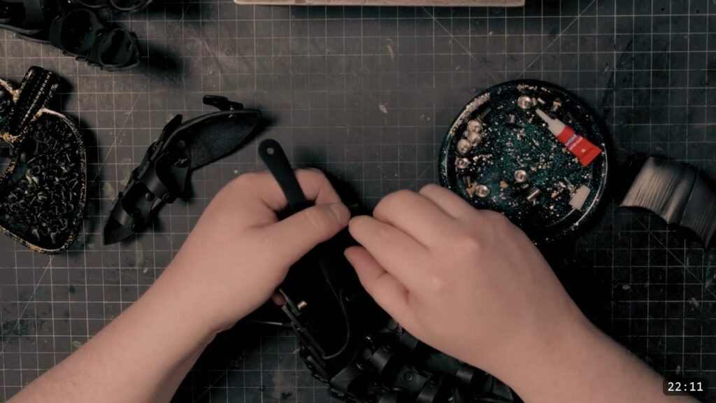 hands setting Chicago screws on the black articulated wrist section, a tray of silver screws and thread lock at the side