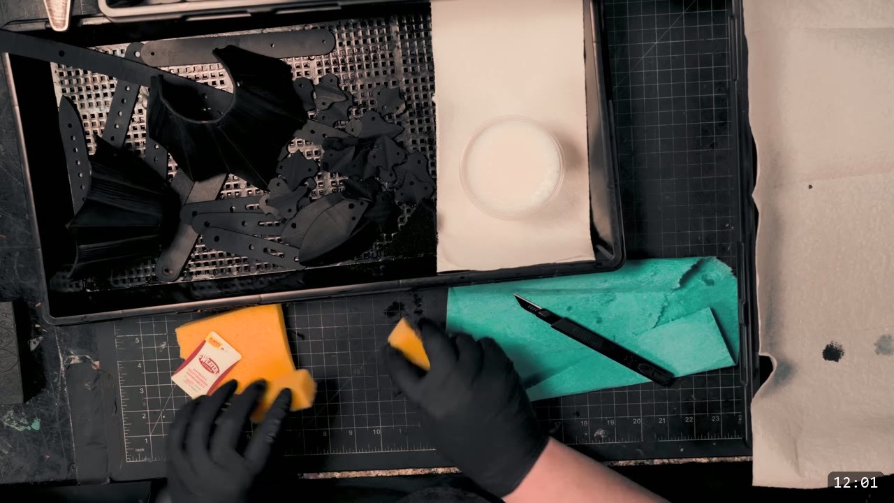 Berserk Gauntlets Build Guide: The Leather Version, Step by Step 10 gloved hands sponging black dye onto leather pieces drying on a mesh rack in a tray, a cup of dye alongside