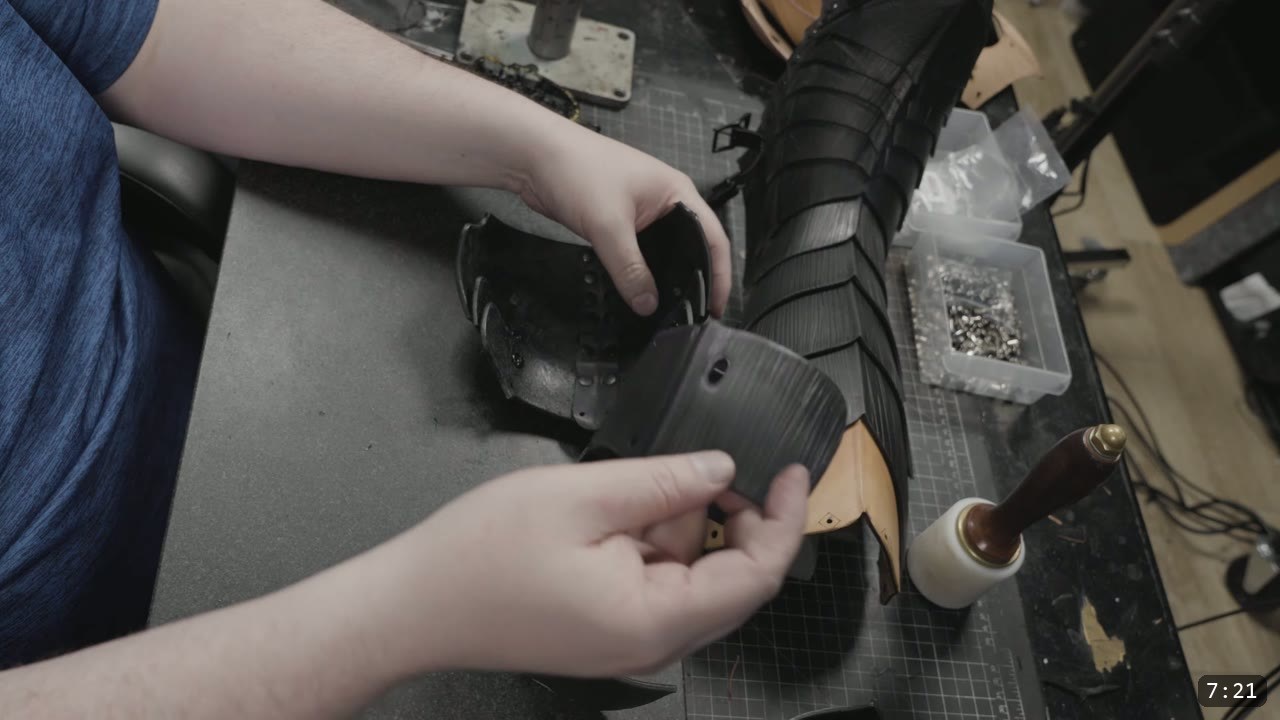 Berserk Greaves Build Guide: Leather Berserker Shin and Calf Armor 12 hands fitting a black fluted calf back plate to the assembled greave, a mallet and hardware bin on the bench