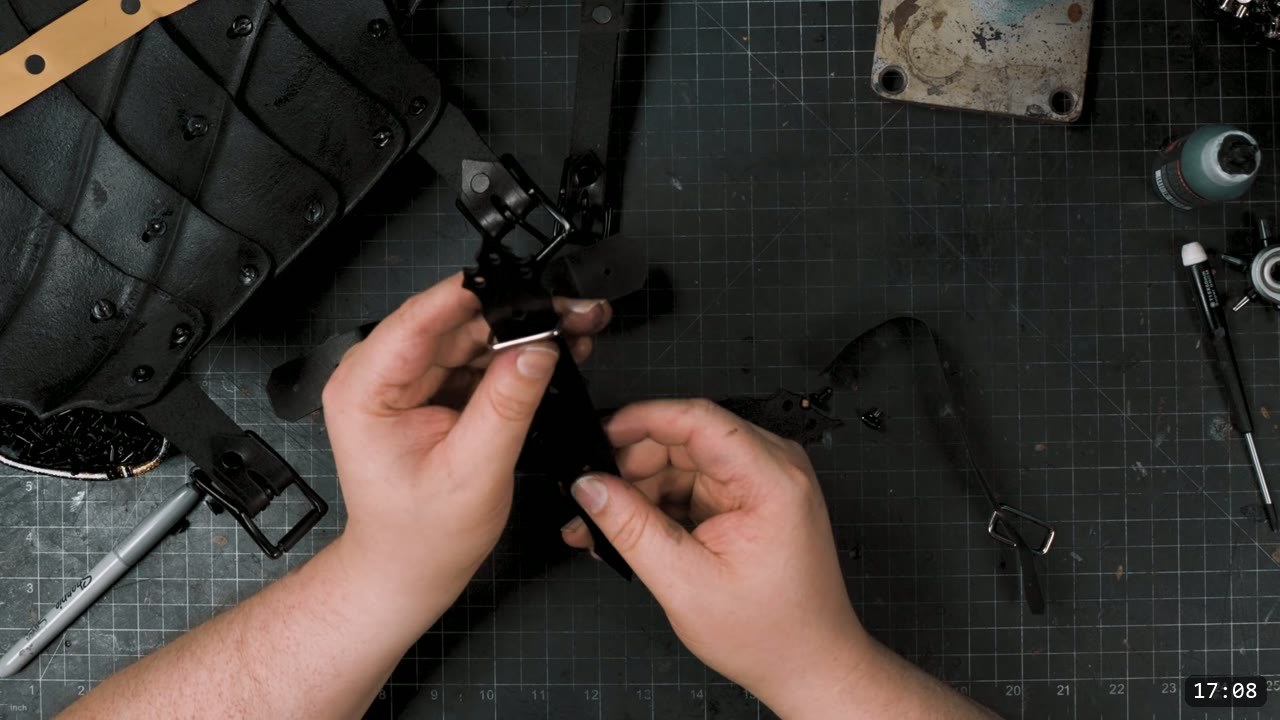 Berserk Leg Armor Build Guide: Articulated Leather Cuisses, Knees, and Greaves 11 Hands fitting a black metal quick release clasp onto black leather straps, with roller buckles and a bottle of finish on the mat