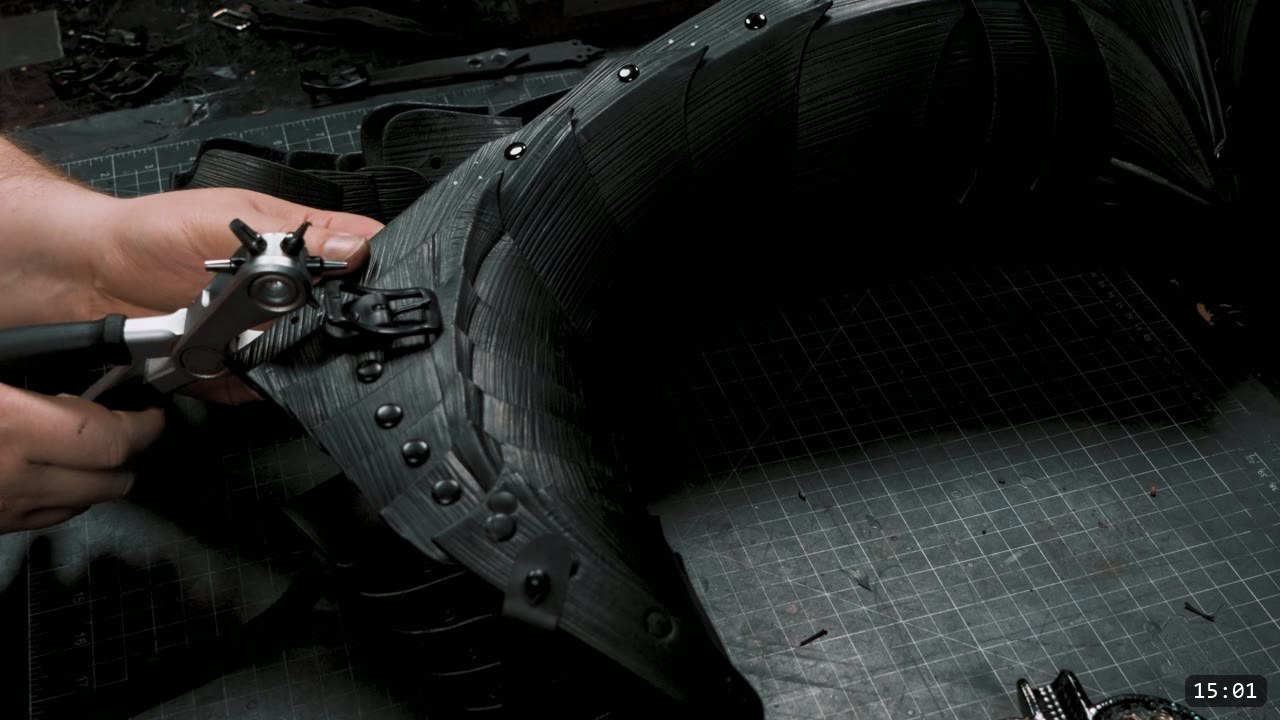 Berserk Leg Armor Build Guide: Articulated Leather Cuisses, Knees, and Greaves 10 The fully assembled dyed black cuisse of overlapping fluted plates, with a hand punching a hole in a black strap using rotary punch pliers