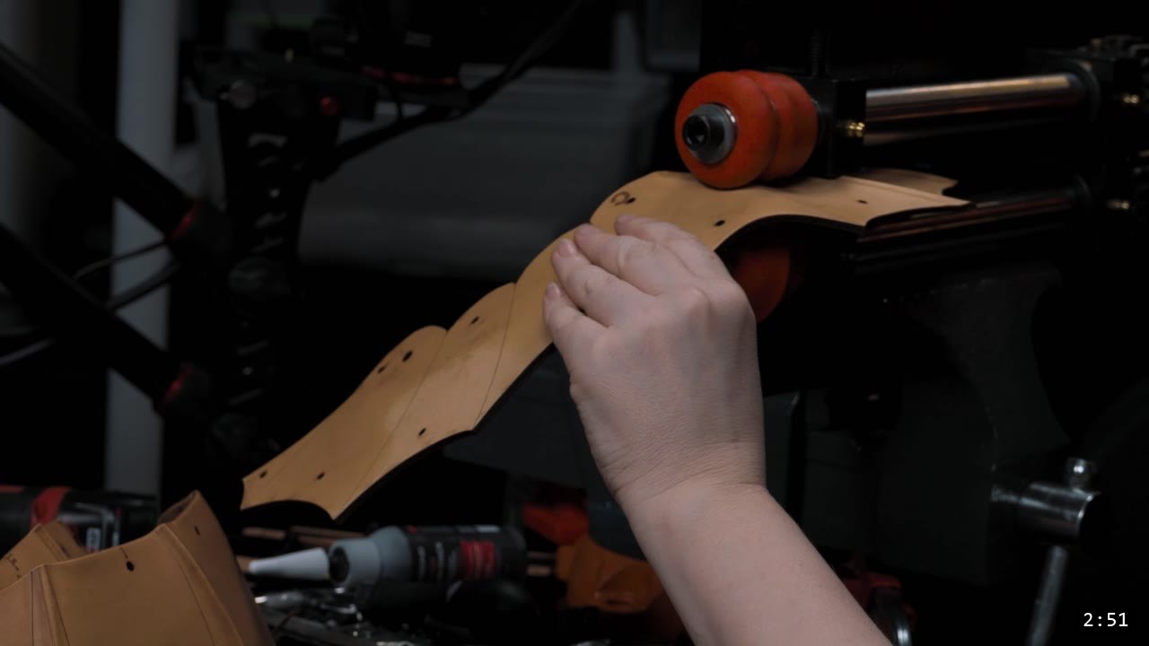 Berserk Leather Pauldrons Build Guide: Articulated Shoulder Armor from the Berserk Suit 5 a hand working a cut tan leather strap over a red forming buck at the workbench