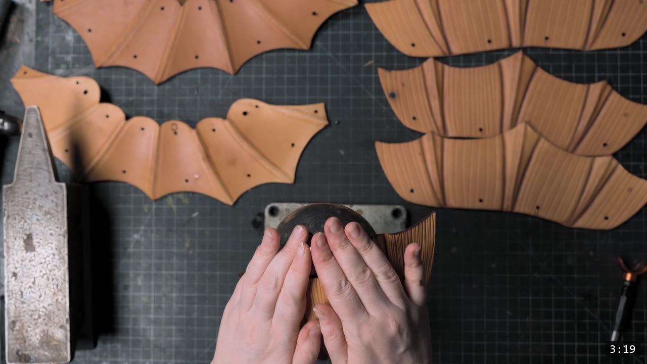 Berserk Leather Pauldrons Build Guide: Articulated Shoulder Armor from the Berserk Suit 6 hands pressing a damp tan pauldron plate over a rounded metal doming stake, with fanned fluted plates and rivet holes arranged on the mat