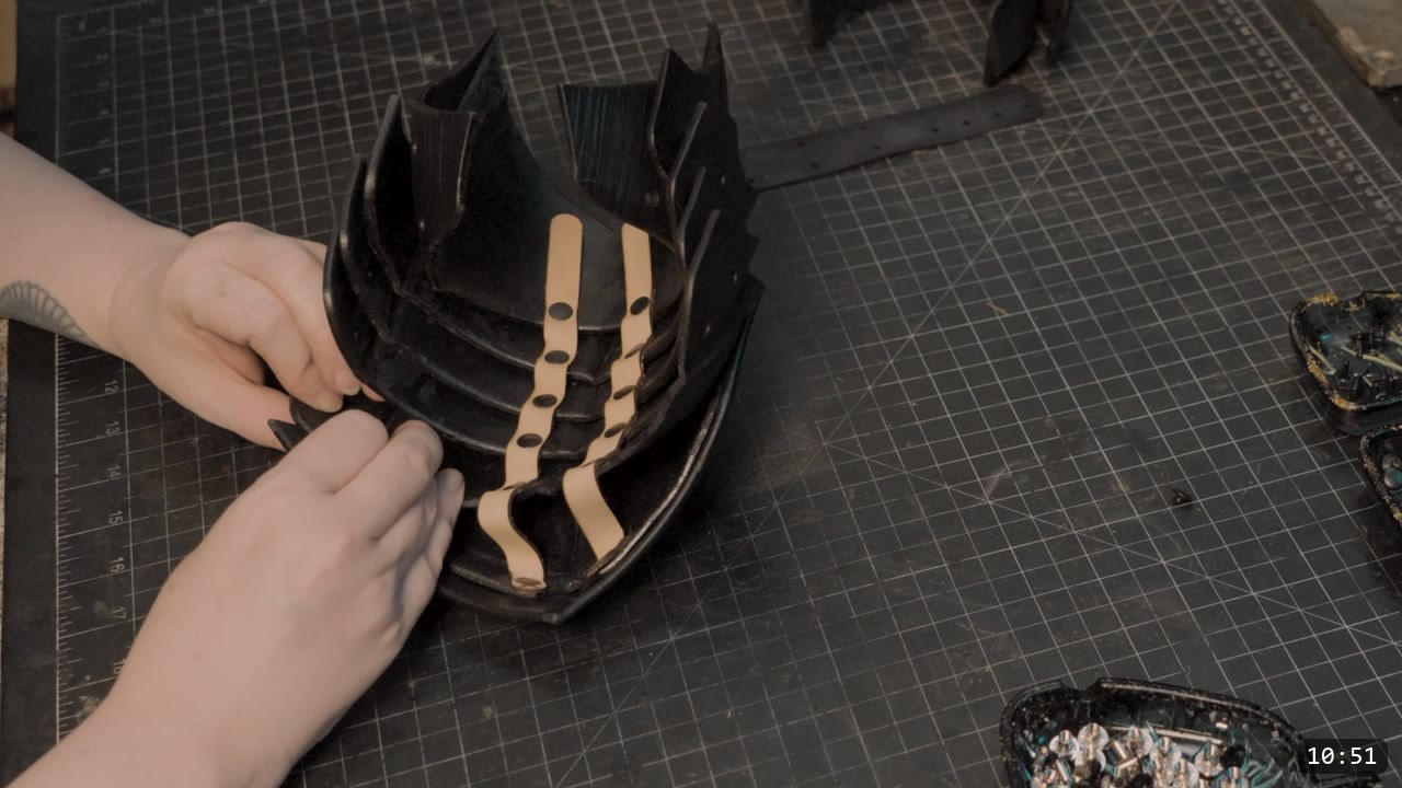 Leather Sabatons Build Guide: Berserk Foot Armor from a Flat Pattern 11 hands threading tan retaining straps through the cupped black heel plates of the sabaton back