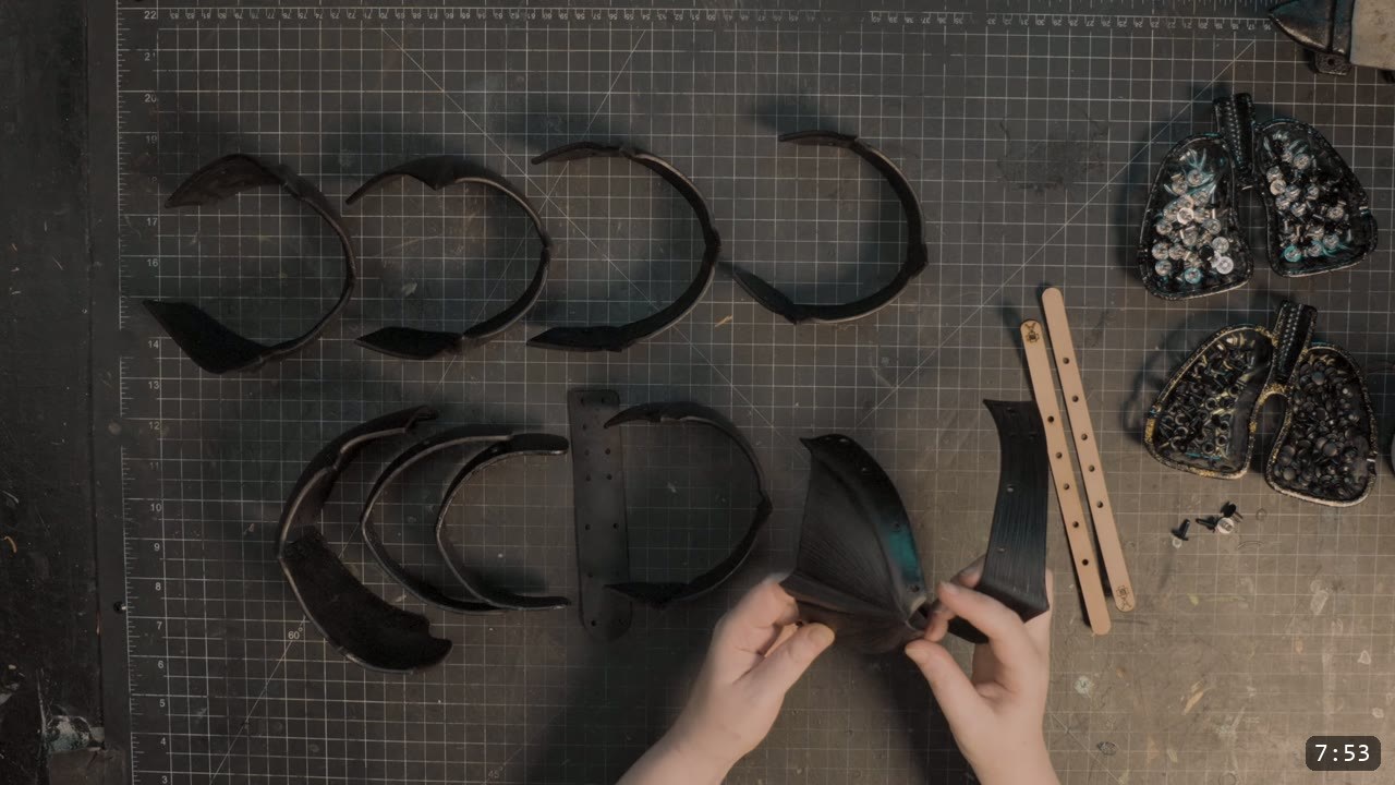 Leather Sabatons Build Guide: Berserk Foot Armor from a Flat Pattern 8 dyed black sabaton plates laid out in order on the cutting mat with a tan retaining strap and trays of rivets and Chicago screws