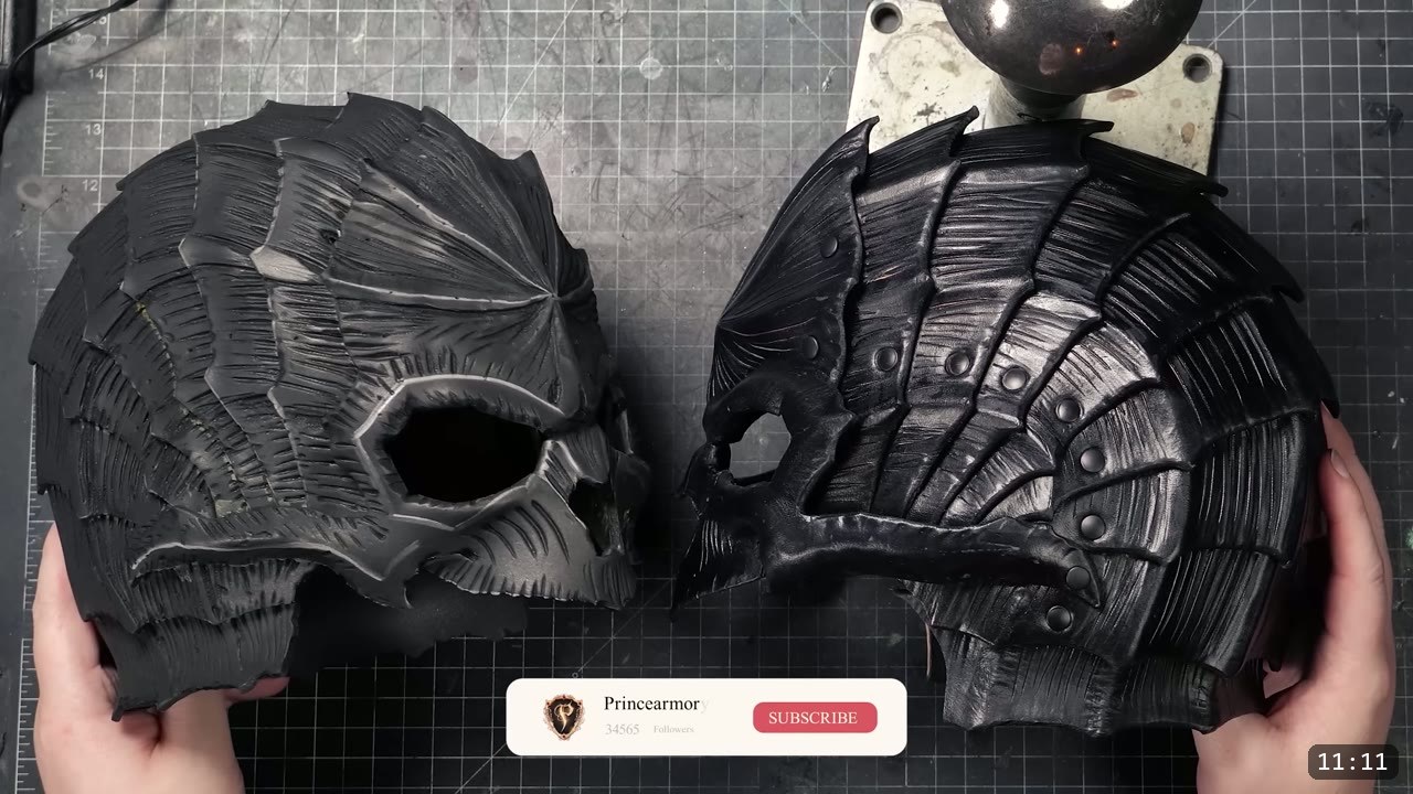 two finished black leather helmets from the Berserk series side by side, the skull helmet on the left and the hound helmet on the right, both built from overlapping textured plates with rivets