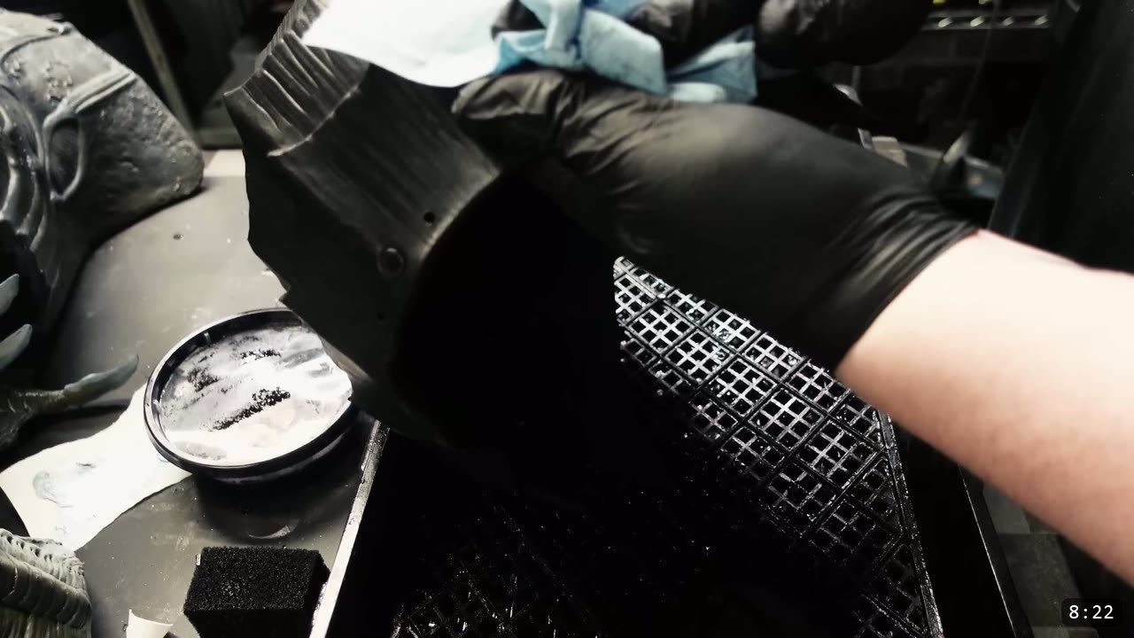 applying finish to the black-dyed helmet with a sponge on a drying grate, a tub of finish beside it