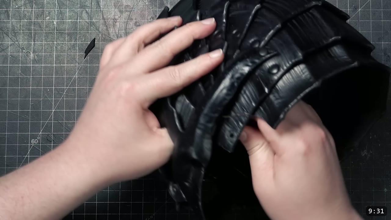 hands shaping and checking the fit of the glossy black-dyed helmet core on the cutting mat