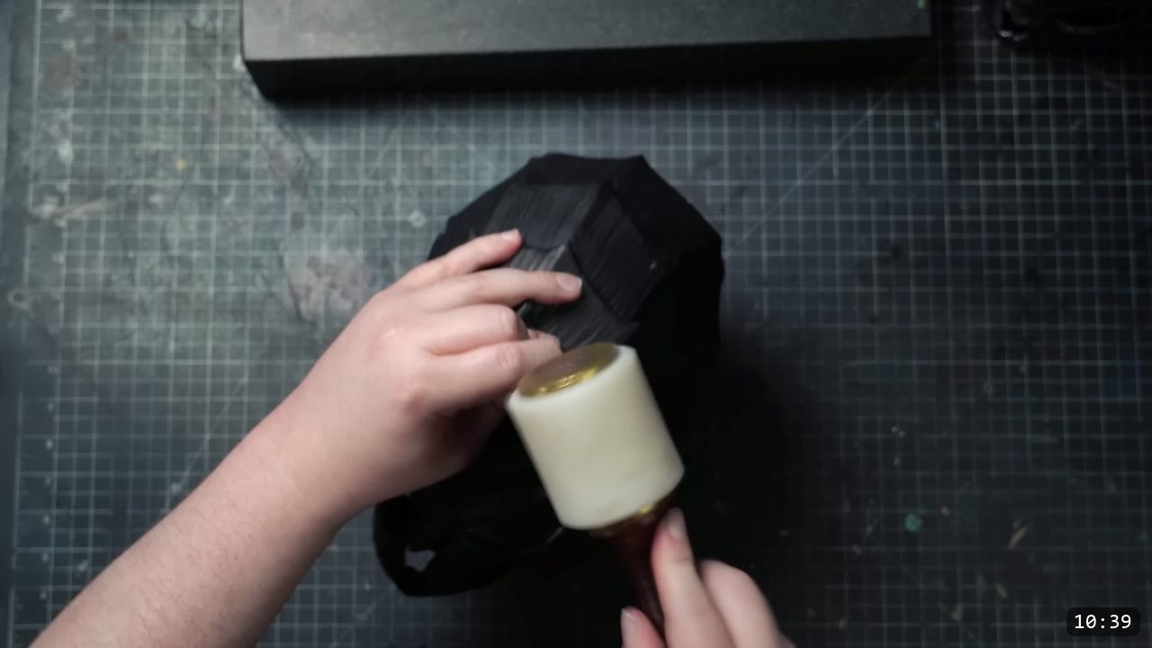 tapping a black-dyed leather piece with a white poly mallet on the cutting mat during faceplate fitting