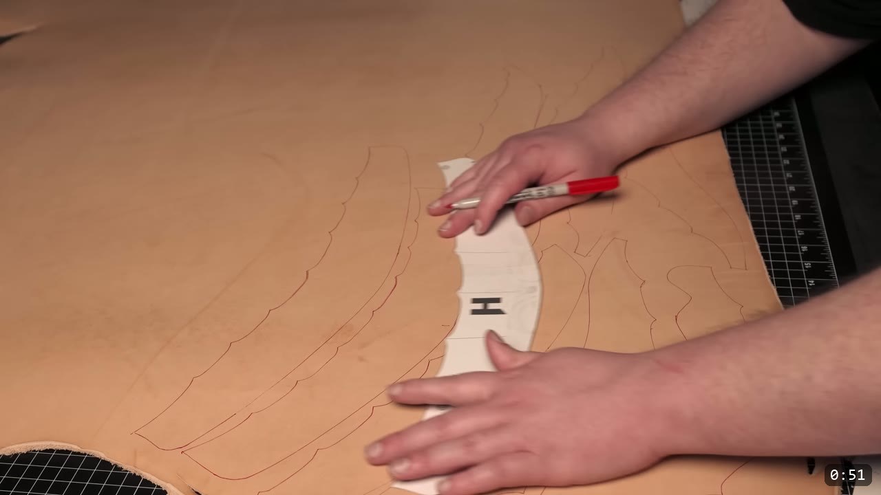 tracing a lettered helmet pattern piece onto natural tan vegetable-tan leather with a red fine-point marker on a cutting mat