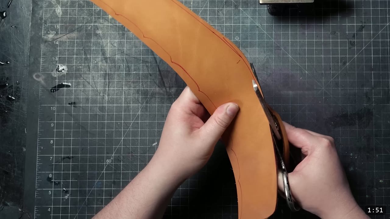 cutting a long curved helmet piece from tan leather with heavy-duty leather shears, following the red traced line