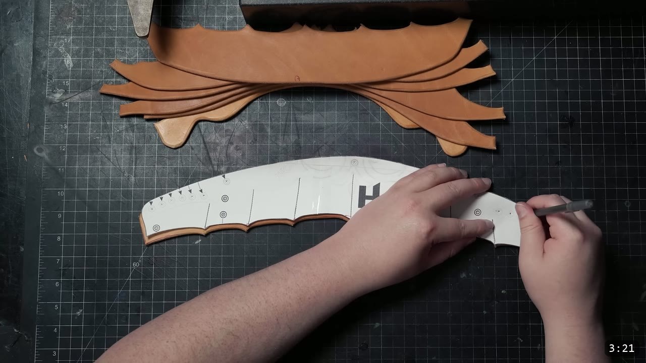 overlaying a white pattern piece on a cut leather part to transfer rivet placements with a stylus, cut straps resting on the mat above