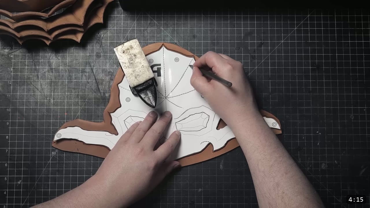 transferring the skull faceplate's design lines from the pattern onto tan leather with a stylus, a metal weight holding the pattern down