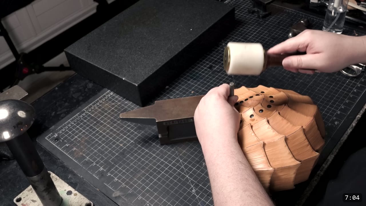 riveting the assembled overlapping-plate core dome over a small anvil, punched rivet holes visible across the plates