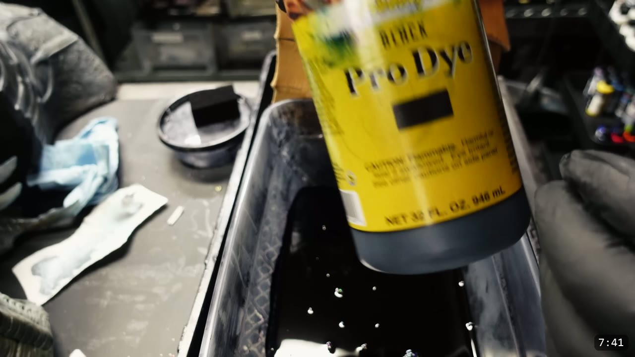 a bottle of black oil dye held over a dye tub for immersion dyeing, sponge and gloves on the bench