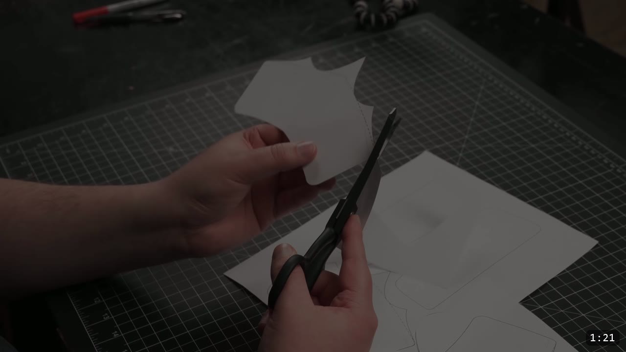 cutting a printed bracer pattern out of paper with scissors on a green cutting mat