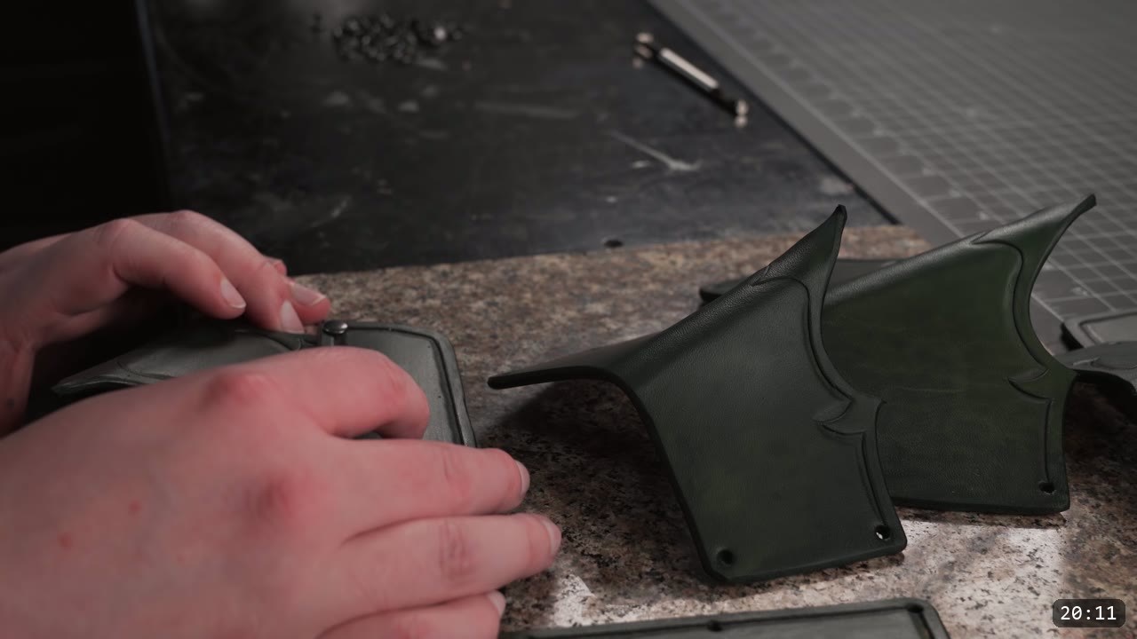 setting rivets to join the dyed green bracer plates, the carved barbed border and center crease visible