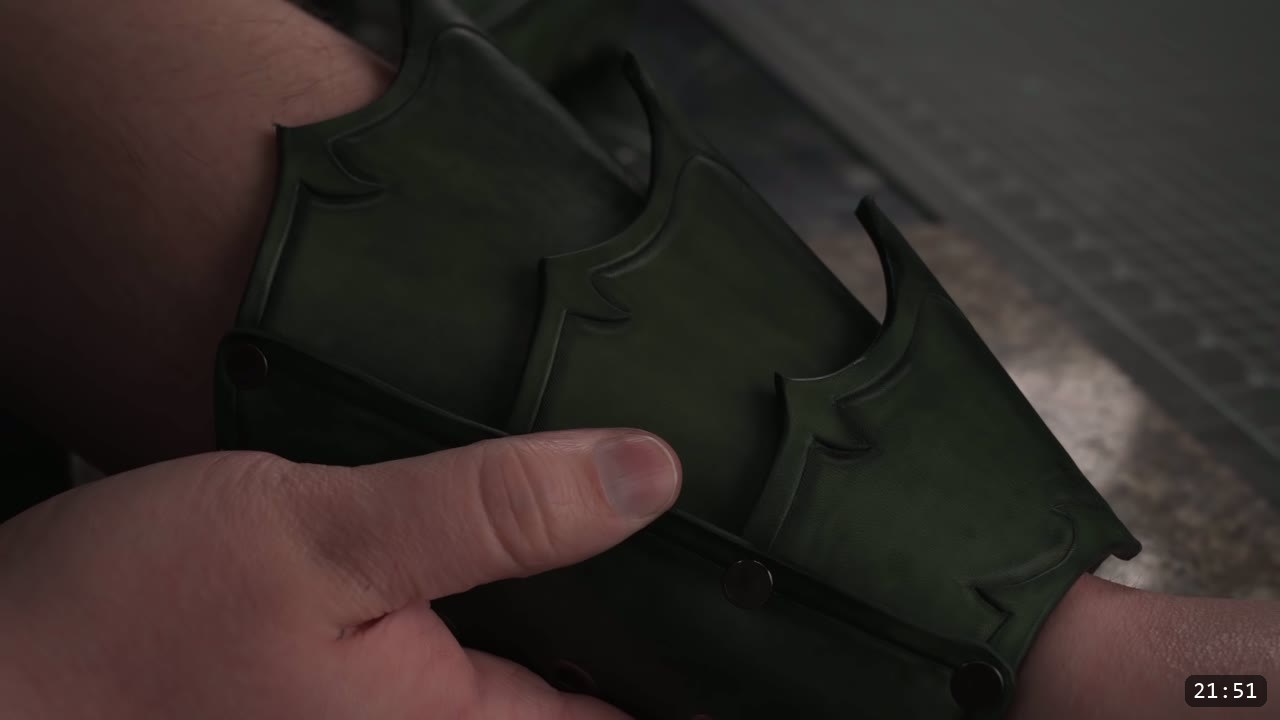 the finished dark green fantasy bracer worn on a forearm, three overlapping carved plates joined by dome rivets