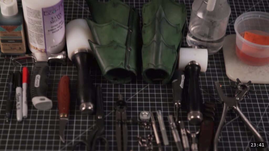 the finished pair of green fantasy bracers surrounded by the markers, maul, swivel knife, slicker, hole punch, dye, and finish used in the build