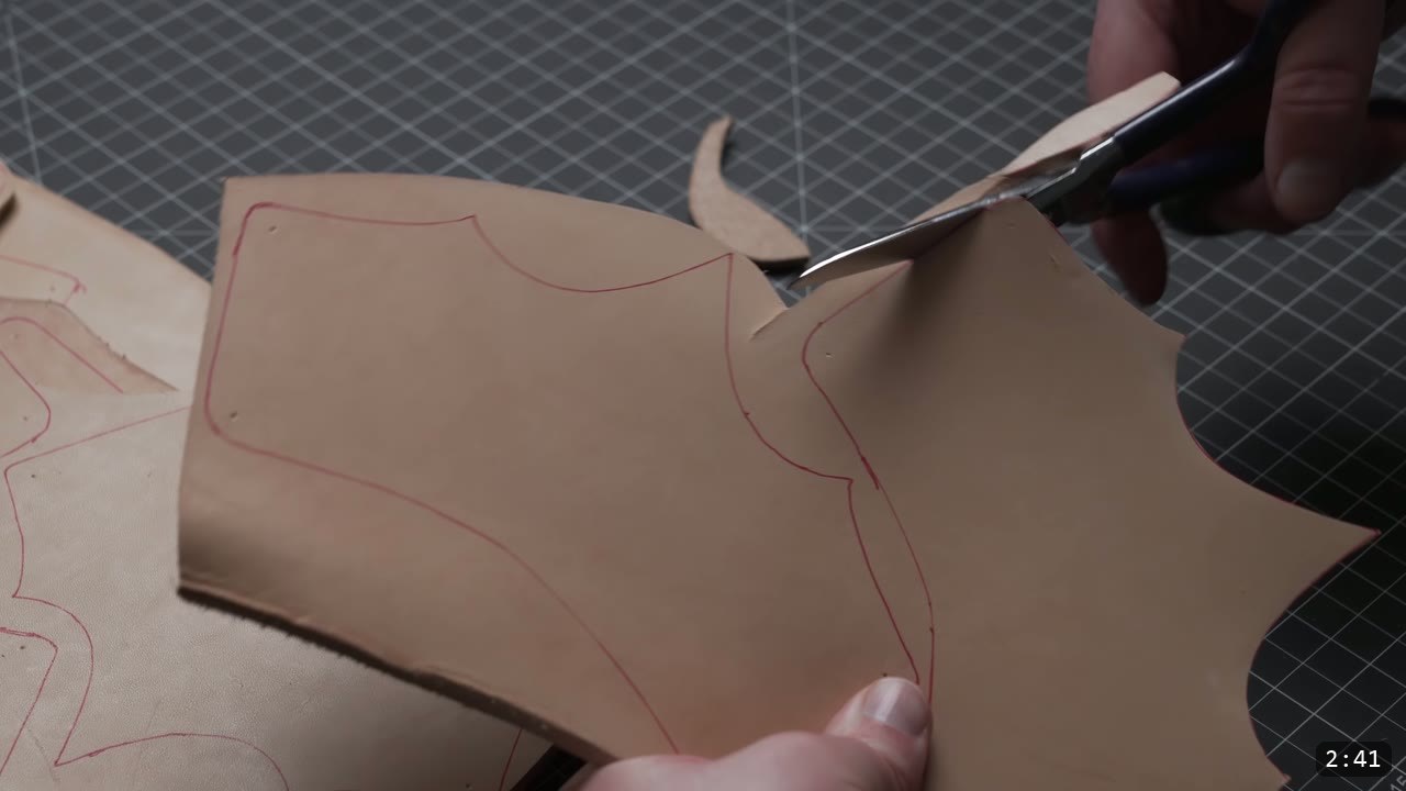 cutting a vegetable-tan bracer piece from the hide with leather shears, following the red traced outline