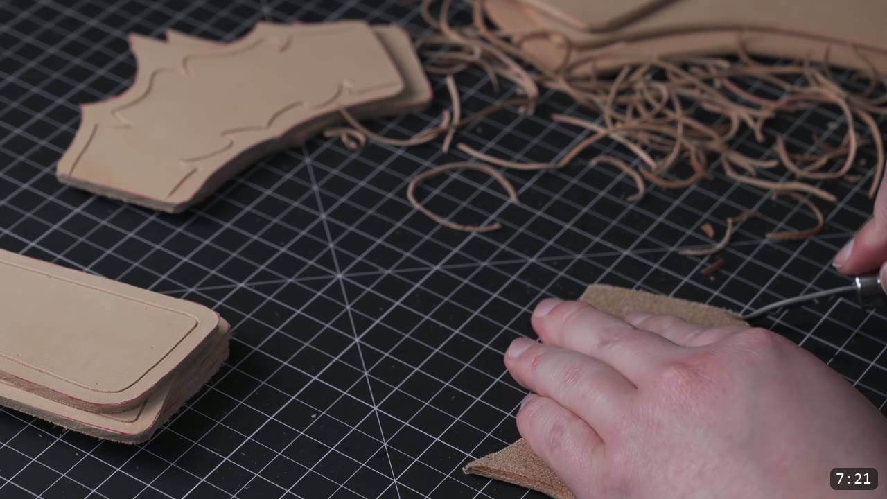 trimming a rounded bevel along the edge of a bracer piece, curled leather shavings on the mat