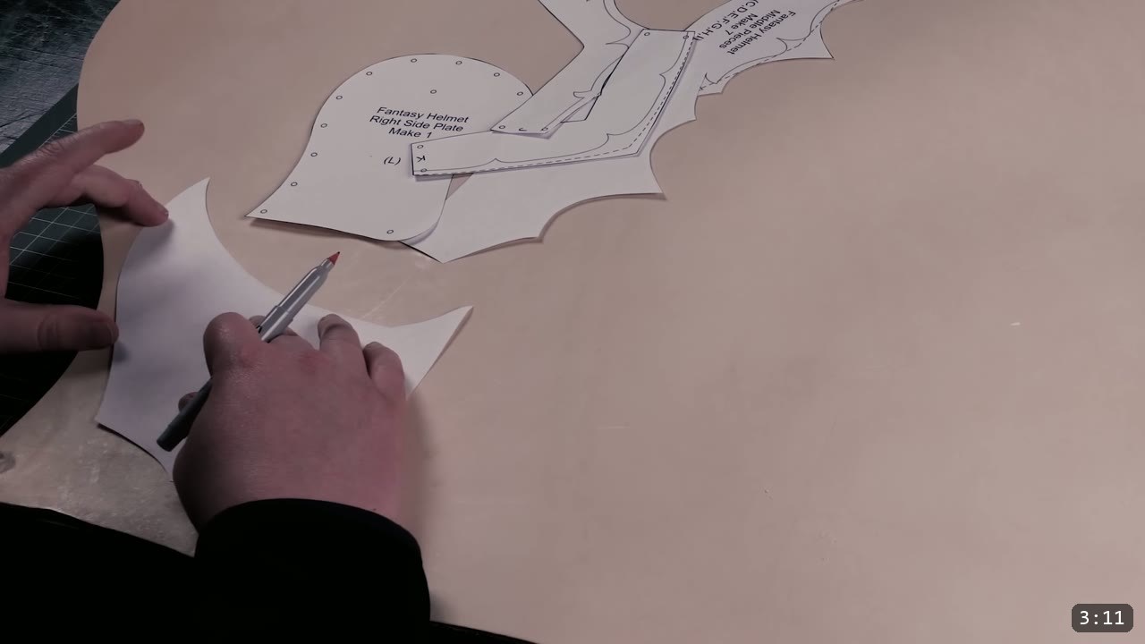 tracing a printed Fantasy Helmet side-plate pattern onto natural tan leather with a red fine-point marker
