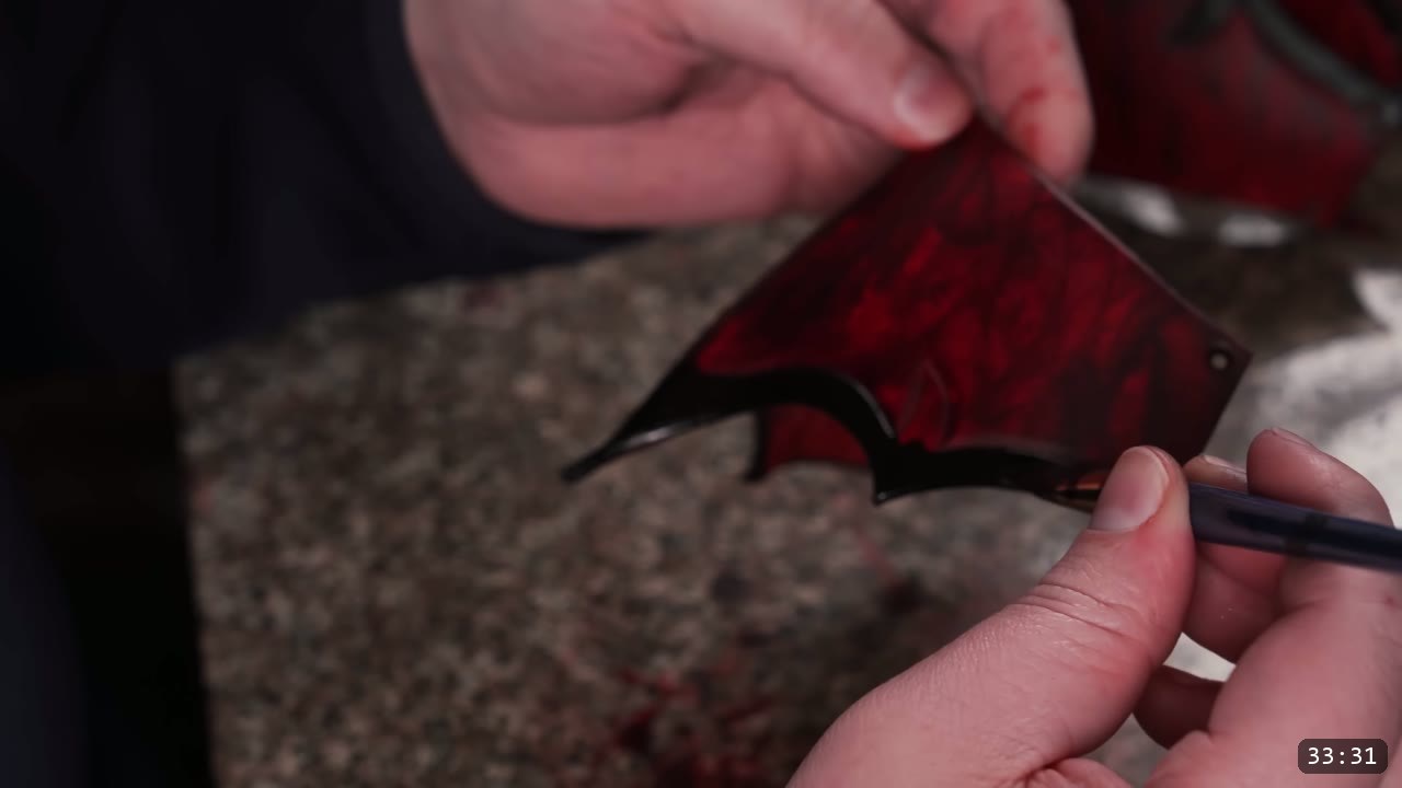 marking a hole location on a marbled red-and-black barbed leather piece with a blue ballpoint pen on a stone slab