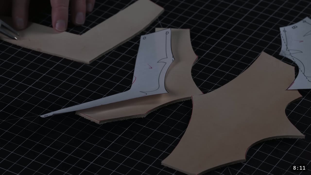 cut tan leather helmet pieces with barbed edges on a black cutting mat, one paper pattern piece still resting on a piece