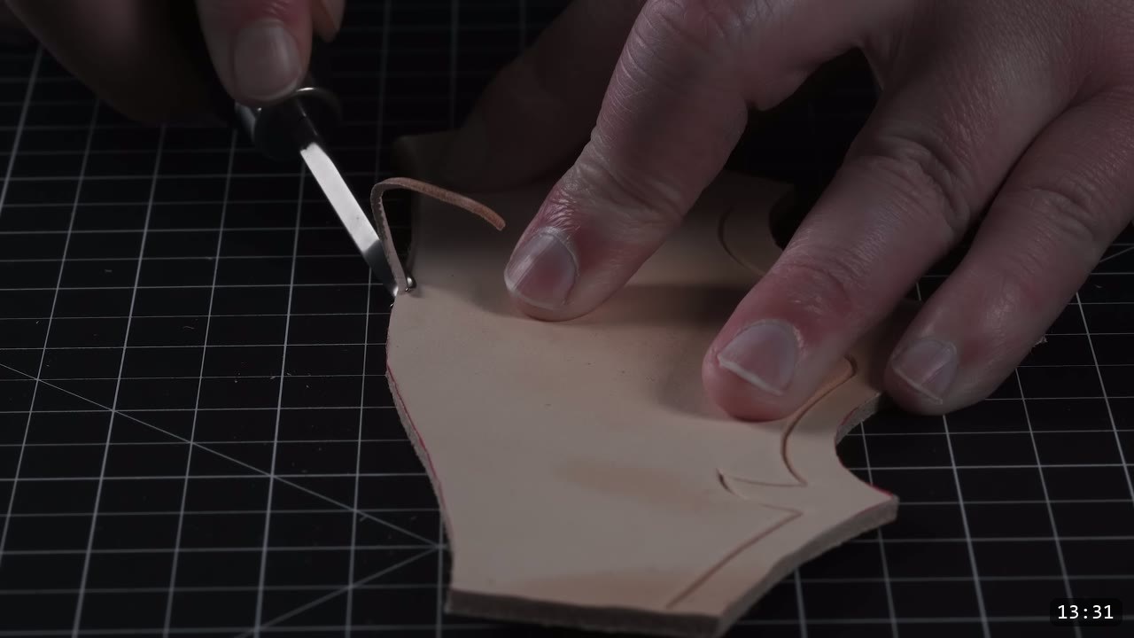 pulling a thin sliver off a leather edge with a hand edge beveler, a carved design line visible along the piece