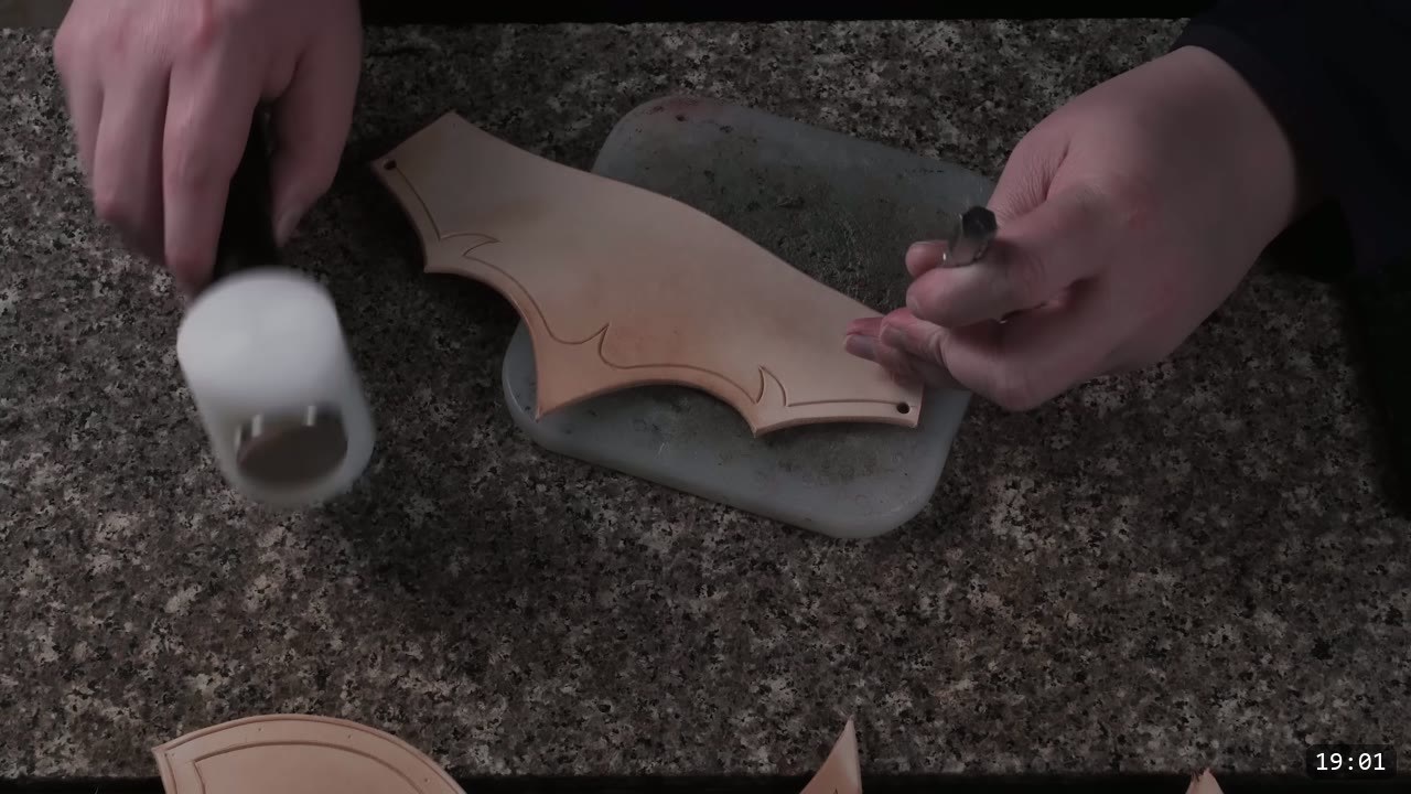 punching a hole in a barbed leather piece on a stone slab with a hand punch and a white poly mallet