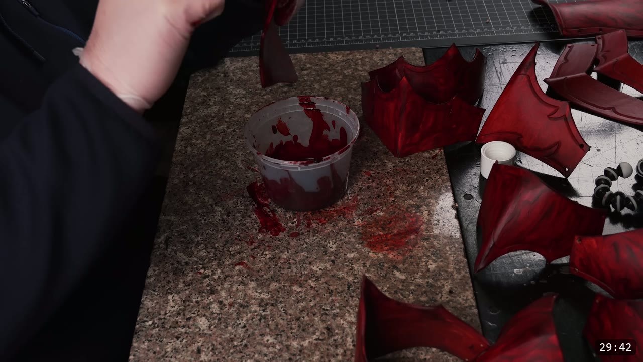 deep marbled-red fantasy helmet pieces with black-trimmed barbed edges laid out to dry beside the dye tub
