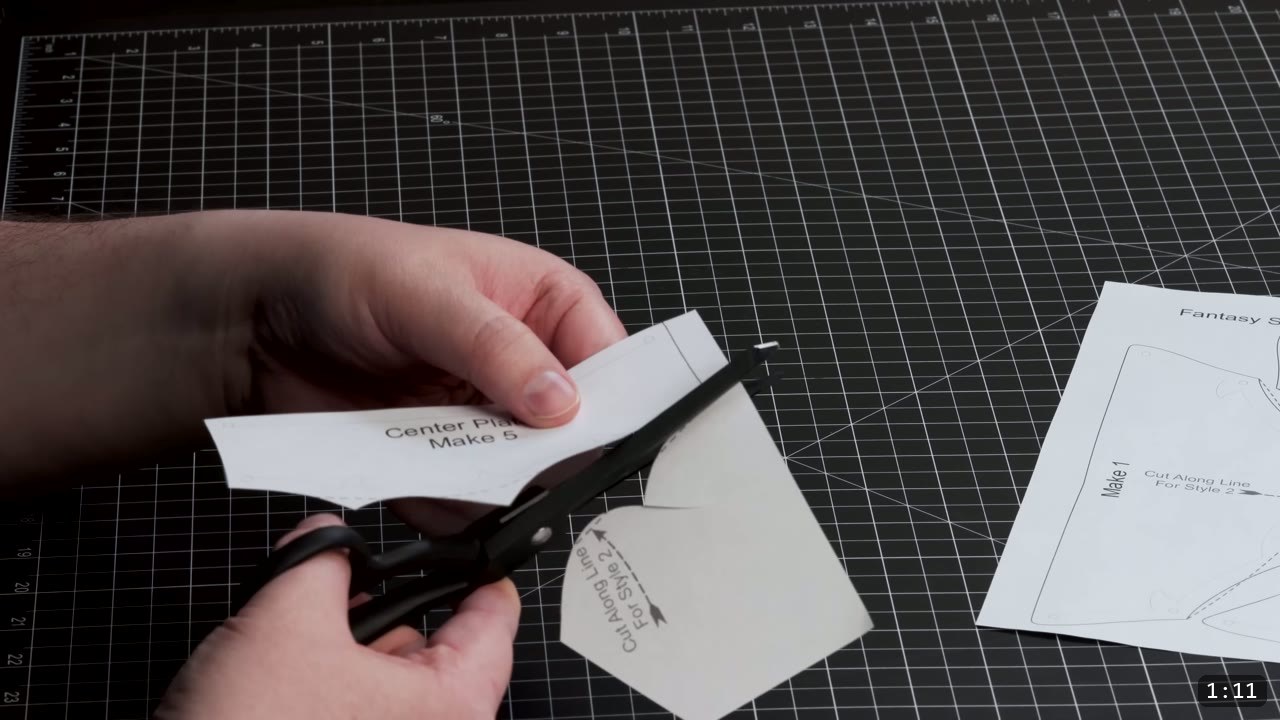 Fantasy Spaulders Build Guide: Leather Shoulder Armor from a Flat Pattern 2 hands trimming a paper spaulder pattern piece labeled Center Plate Make 5 with scissors on a gridded cutting mat, a second Fantasy pattern sheet beside it