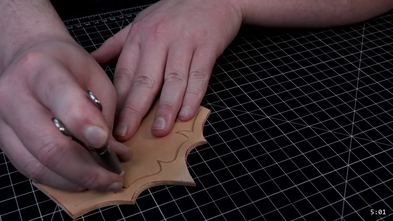 Fantasy Spaulders Build Guide: Leather Shoulder Armor from a Flat Pattern 5 a swivel knife carving a curved design line into a barbed tan leather plate held flat on the cutting mat