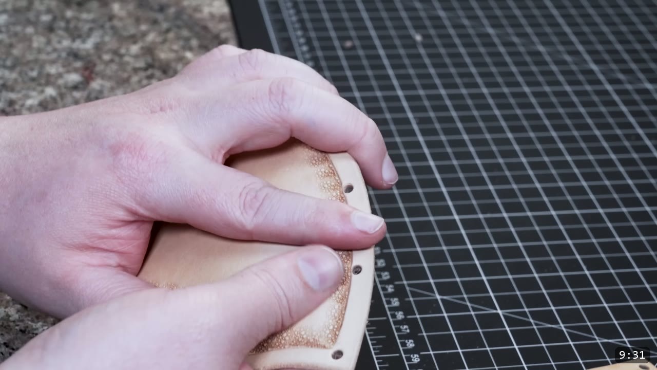 Fantasy Spaulders Build Guide: Leather Shoulder Armor from a Flat Pattern 7 hands working a curved tan plate that has a line of punched edge holes, resting on the cutting mat